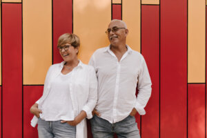 A older couple is seen happily posing in front of a wall.