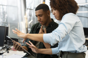 An image of two people looking into an ipad while in an office setting.