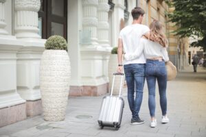 a couple walks toward airport with luggage in tow