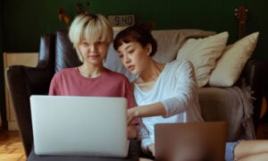 Two women sit on the floor with laptops researching HISA rates