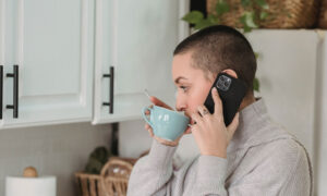 a woman on her phone in the kitchen, possibly answering a call from a debt collector about a family member