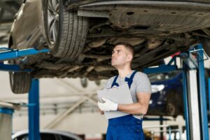 Mechanic with a clipboard stands under a hoisted car