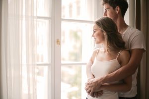 young couple looks out window of their home after purchasing home insurance