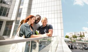 Three people stand outside a condo tower and sign paperwork