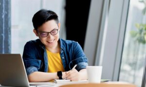 A smiling young man takes notes about his G I C returns in a cafe