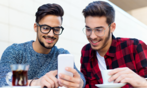 Two young people at a cafe smile at a smartphone.