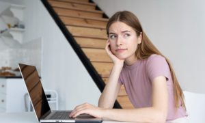 A young woman with her hand on her laptop and a puzzled expression