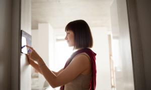 A young woman adjusts the temperature on a home thermostat