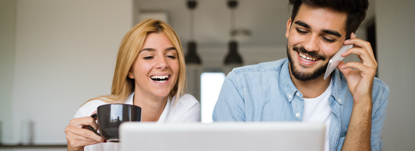 A woman (left) laughs while holding a cup of coffee and a man smiles while talking on the phone.